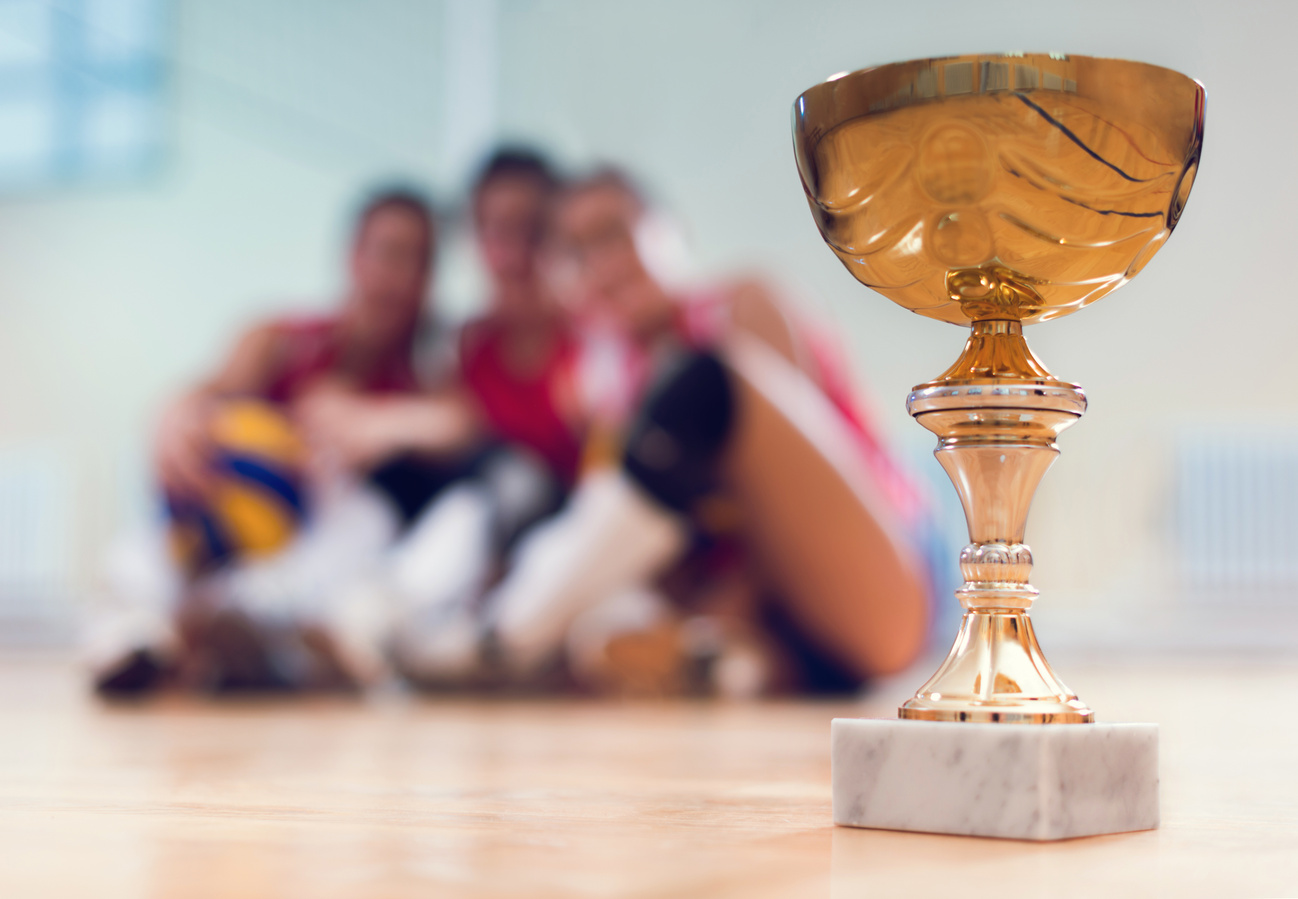 Volleyball champion trophy with volleyball players in background.